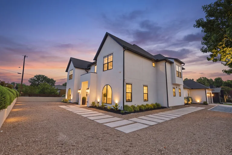 Illuminated garage-side exterior and driveway at dusk at 3860 Walnut Hill Lane in Dallas