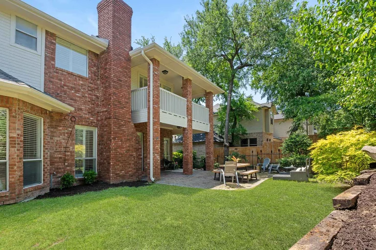 Backyard lawn and brick rear exterior beneath mature trees — FLM media library example
